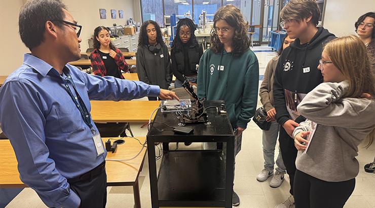 A group of high school students watching Dr. Pengcheng Lv give a presentation on a robotic arm